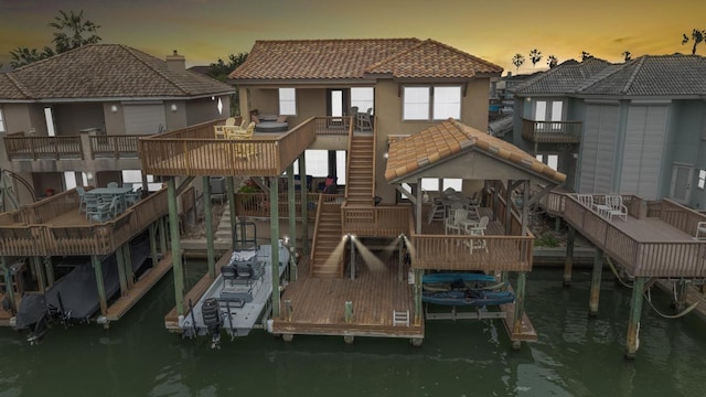 back of house featuring a tile roof, a water view, stairway, and stucco siding