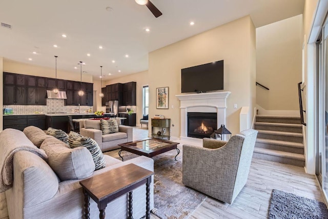 living area with ceiling fan, recessed lighting, light wood-style floors, stairway, and a glass covered fireplace