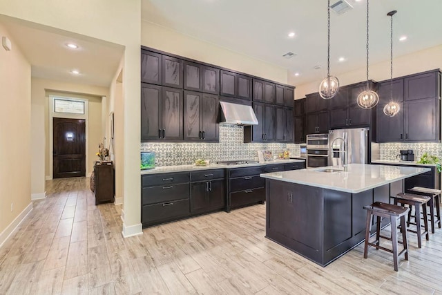 kitchen with visible vents, a breakfast bar area, stainless steel appliances, light countertops, and exhaust hood