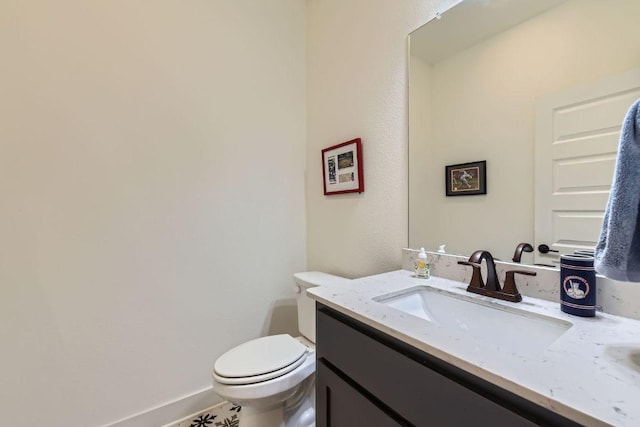 half bathroom featuring toilet, baseboards, and vanity