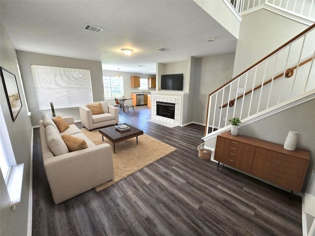 living room featuring visible vents, baseboards, stairs, a fireplace, and dark wood-style flooring