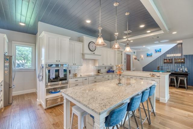 kitchen featuring decorative backsplash, light wood-style flooring, a peninsula, stainless steel appliances, and white cabinetry