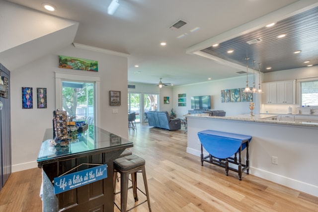 kitchen with light wood-style floors, visible vents, a kitchen breakfast bar, and white cabinetry