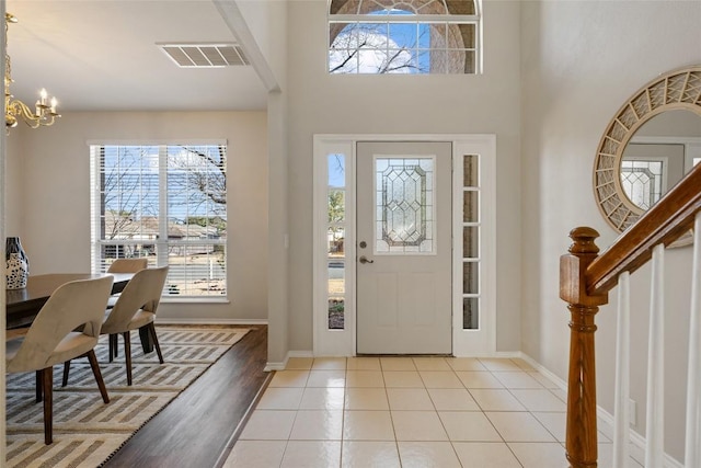 tiled foyer entrance featuring visible vents, a high ceiling, a chandelier, baseboards, and stairs