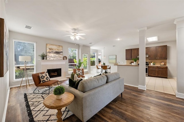 living area with visible vents, ceiling fan, wood finished floors, a tile fireplace, and baseboards