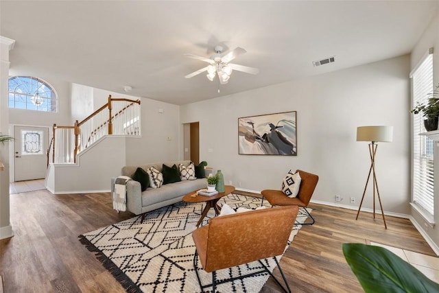 living area featuring wood finished floors, a ceiling fan, visible vents, stairs, and baseboards