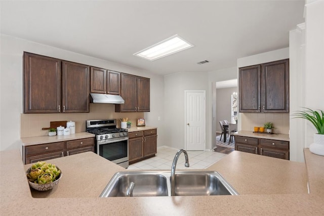 kitchen with light countertops, stainless steel range with gas stovetop, a sink, and under cabinet range hood