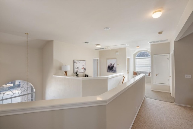 hall with carpet floors, baseboards, visible vents, and an upstairs landing