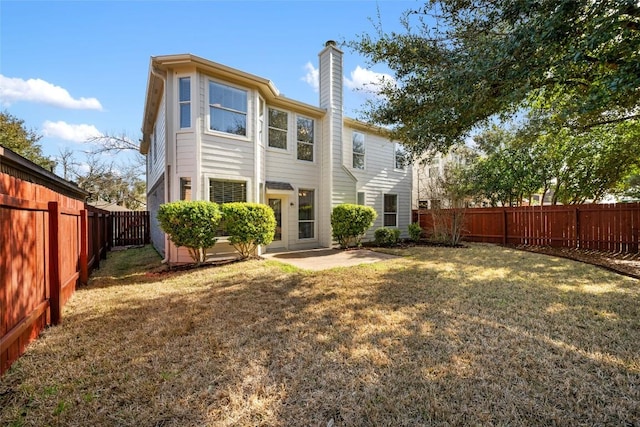 back of house with a patio area, a fenced backyard, a yard, and a chimney