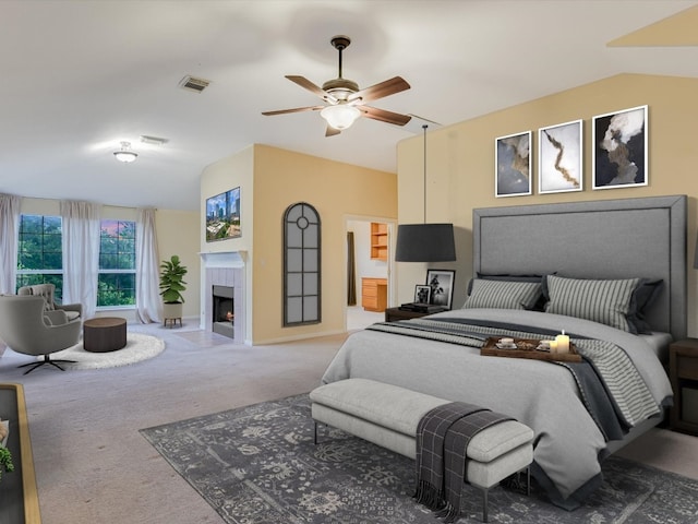 carpeted bedroom with visible vents, vaulted ceiling, a fireplace, ensuite bathroom, and a ceiling fan