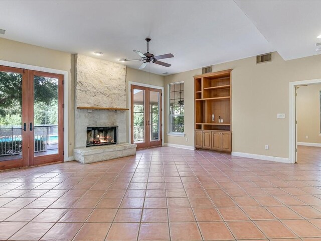 unfurnished living room with a stone fireplace, light tile patterned flooring, french doors, and visible vents