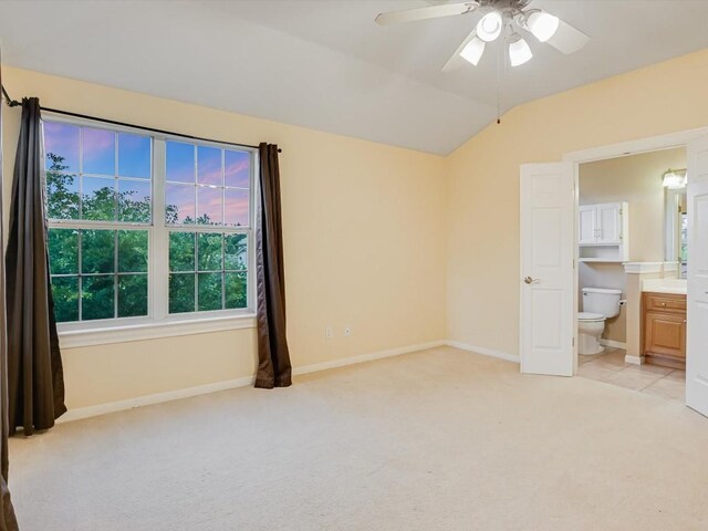 unfurnished bedroom featuring ensuite bathroom, baseboards, light colored carpet, ceiling fan, and vaulted ceiling