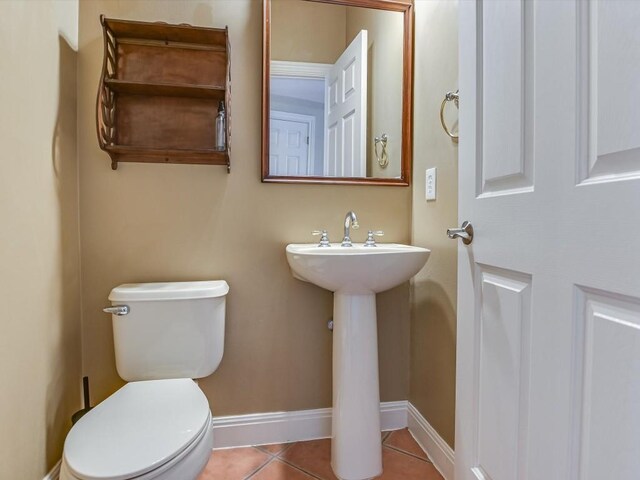 half bath featuring tile patterned flooring, toilet, baseboards, and a sink