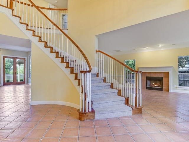 stairs with baseboards, a high ceiling, a tile fireplace, tile patterned flooring, and french doors