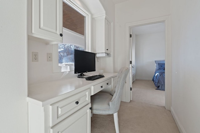 office area featuring light carpet, built in desk, and baseboards