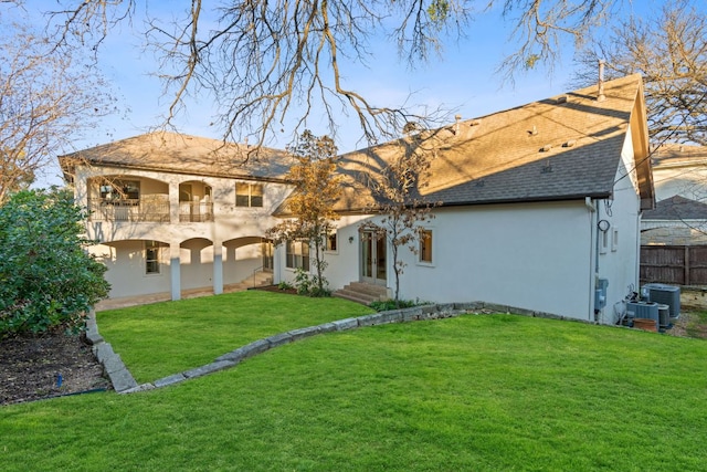 rear view of house featuring entry steps, a balcony, central AC, a shingled roof, and a yard