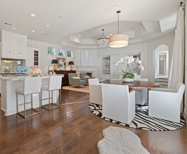 dining space with visible vents, a raised ceiling, arched walkways, dark wood-style floors, and a lit fireplace