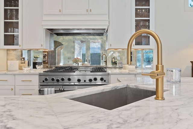 kitchen with glass insert cabinets, white cabinetry, stainless steel range, and light stone counters