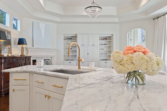 kitchen featuring light stone countertops, a tray ceiling, crown molding, white cabinetry, and a sink