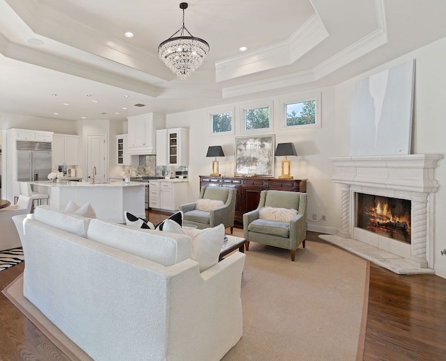 living area with a warm lit fireplace, recessed lighting, wood finished floors, a tray ceiling, and crown molding