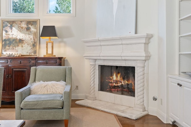 living area featuring a warm lit fireplace, wood finished floors, and baseboards