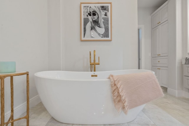 full bathroom with marble finish floor, a freestanding tub, and baseboards