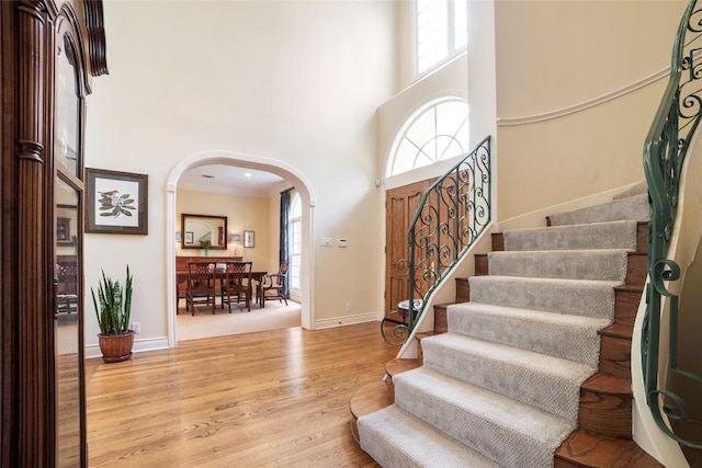 foyer with arched walkways, wood finished floors, a towering ceiling, baseboards, and stairway