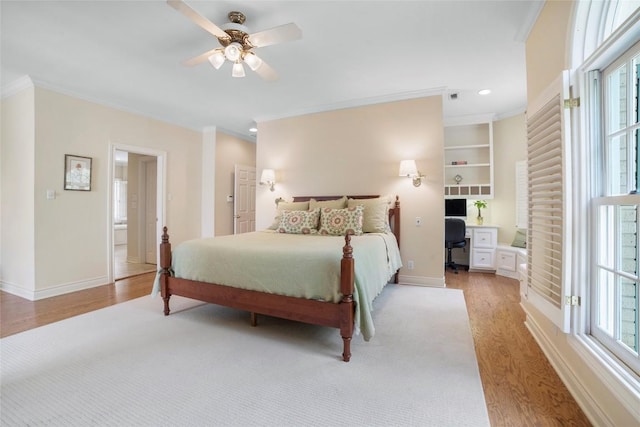 bedroom with light wood finished floors, baseboards, ceiling fan, crown molding, and built in desk