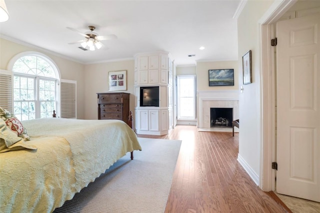 bedroom featuring light wood-style floors, a fireplace with flush hearth, multiple windows, and ornamental molding