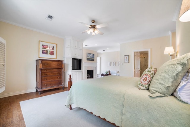 bedroom with a fireplace, wood finished floors, visible vents, baseboards, and crown molding