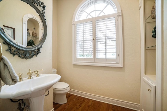 half bath featuring wood finished floors, toilet, and baseboards