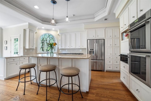 kitchen featuring stainless steel appliances, a tray ceiling, white cabinetry, and light wood-style flooring