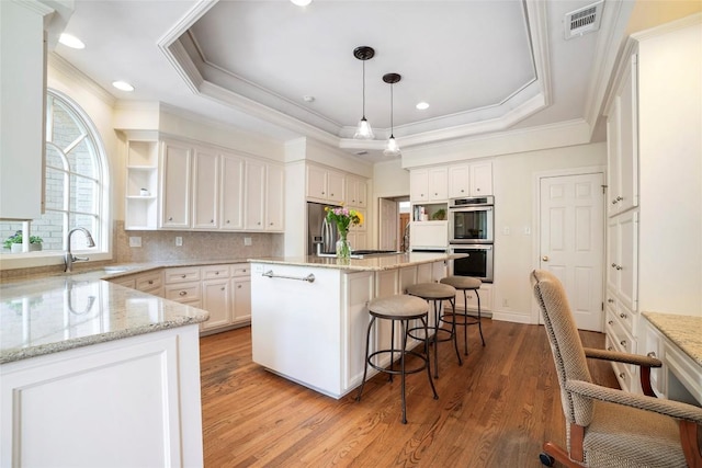 kitchen with a tray ceiling, a breakfast bar, visible vents, appliances with stainless steel finishes, and a sink