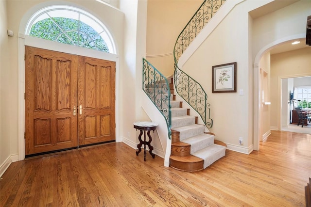 foyer entrance featuring arched walkways, a high ceiling, wood finished floors, baseboards, and stairs