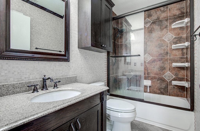 bathroom featuring toilet, combined bath / shower with glass door, tile walls, and vanity