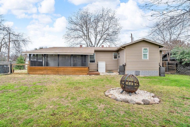 rear view of house with a fire pit, a lawn, a sunroom, fence, and central AC