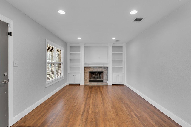 unfurnished living room featuring built in shelves, a fireplace, visible vents, and baseboards