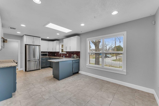 kitchen with stainless steel appliances, tasteful backsplash, a sink, and white cabinets