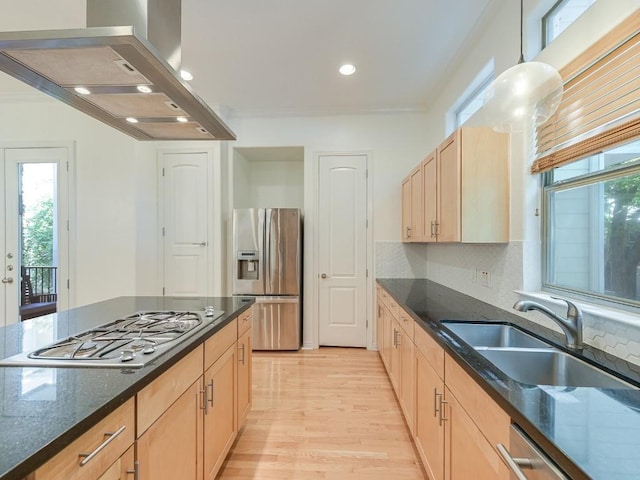 kitchen featuring stainless steel appliances, light brown cabinetry, a healthy amount of sunlight, a sink, and wall chimney range hood