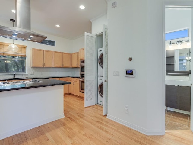 kitchen with light brown cabinets, stacked washer / dryer, light wood finished floors, dark countertops, and island exhaust hood