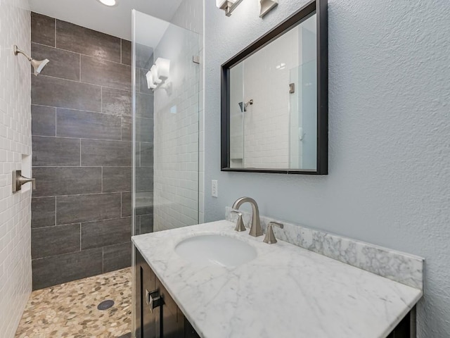 bathroom featuring a textured wall, a tile shower, and vanity