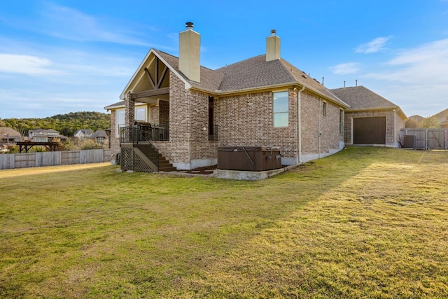 back of property with a yard, brick siding, fence, and a hot tub