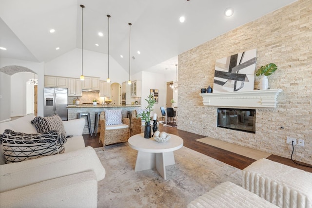 living room with light wood finished floors, arched walkways, a glass covered fireplace, high vaulted ceiling, and recessed lighting