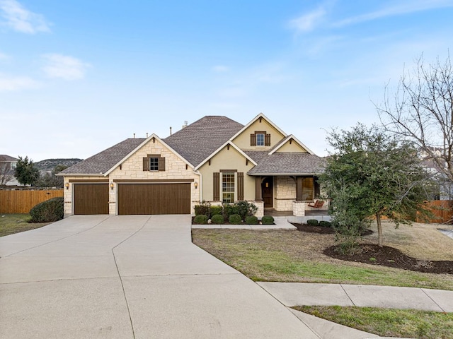 view of front facade featuring driveway, a shingled roof, stone siding, covered porch, and fence