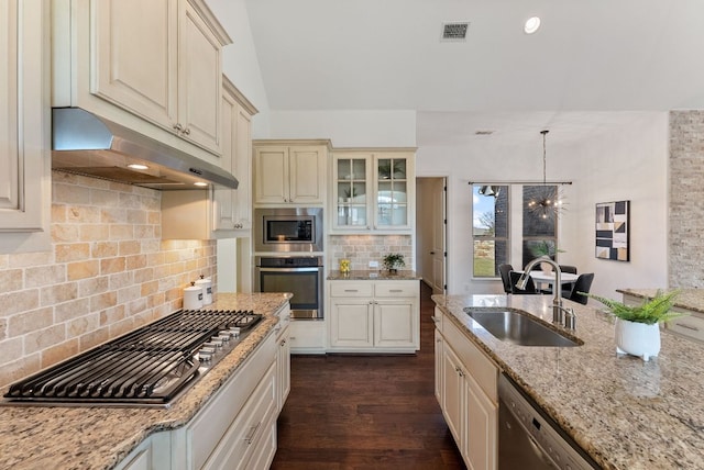 kitchen featuring visible vents, stainless steel appliances, cream cabinetry, under cabinet range hood, and a sink