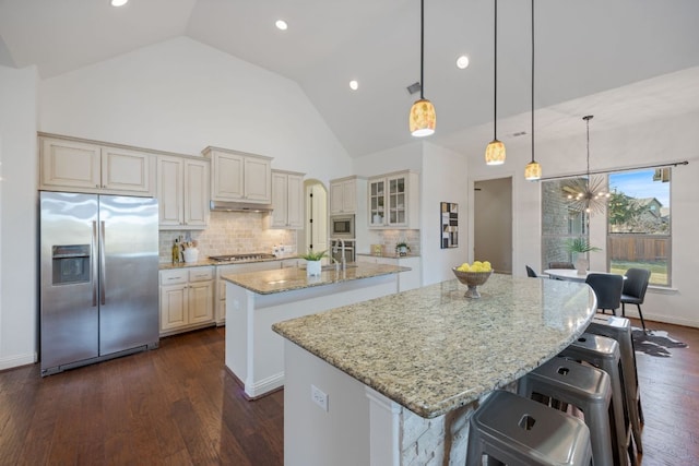 kitchen featuring stainless steel appliances, dark wood finished floors, a center island with sink, and cream cabinets