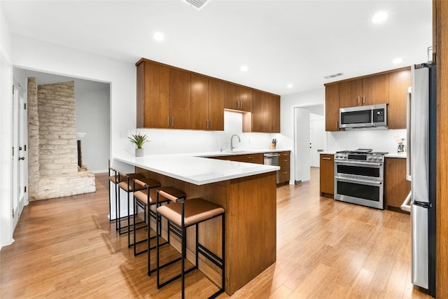 kitchen with a peninsula, light wood-style flooring, tasteful backsplash, and stainless steel appliances