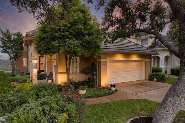 view of front facade with an attached garage, driveway, a tile roof, and stucco siding