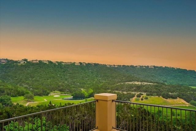 balcony at dusk featuring a wooded view