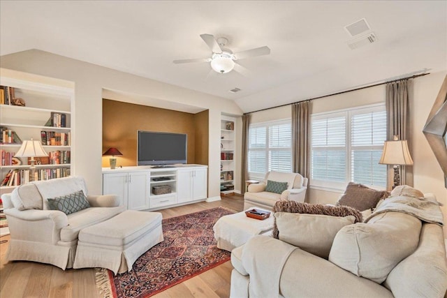 living room featuring built in shelves, visible vents, light wood-style flooring, vaulted ceiling, and ceiling fan